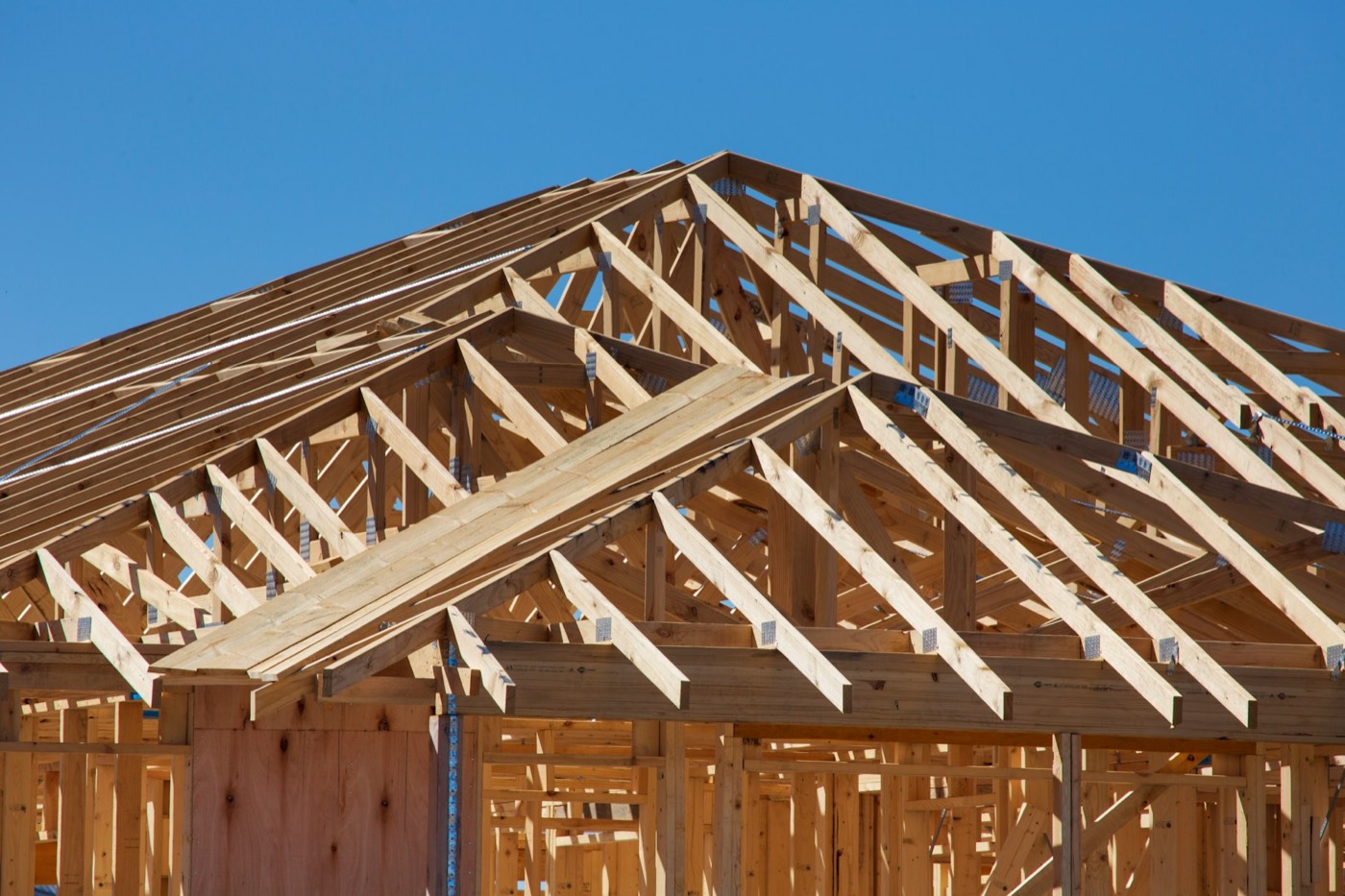 Wood-frame roof trusses on a new build against a clear blue sky